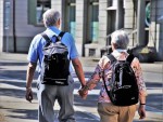 Older couple with back packs holding hands walking away from camera